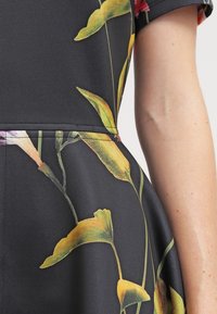 Robe noire avec un imprimé floral jaune et rose, dotée d'un corsage ajusté et d'une jupe évasée. Fabriquée en tissu lisse et extensible.