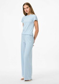 Ljusblå randig loungewear-set som består av en åtsittande kortärmad topp och vida byxor, tillverkad av mjukt bomullsmaterial.