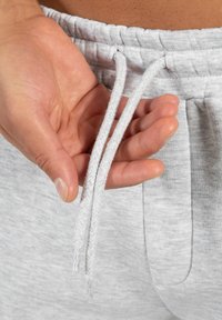 Jasnoszare spodnie dresowe z sznurkiem. Sznurek jest pleciony i lekko postrzępiony na końcach. Tkanina wygląda na miękką i strukturalną.