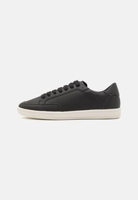 Schwarzer Low-Top-Sneaker mit perforiertem Leder-Obermaterial, schwarzen Schnürsenkeln und weißer Gummisohle vor einem neutralen Hintergrund.