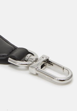 Czarny skórzany pasek przymocowany do błyszczącego srebrnego metalowego karabińczyka z wygrawerowanym napisem "Michael Kors" na białym tle.