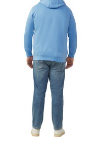 Hellblauer Hoodie mit Kängurutasche und Zugkordelkapuze, kombiniert mit hellblauen Jeans und weißen Turnschuhen, von hinten betrachtet.