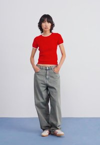 Red ribbed short-sleeve top with white trim paired with loose-fitting gray jeans. Model wears white sneakers with red accents.