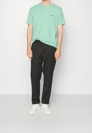 Minzgrünes Baumwoll-T-Shirt mit schwarzem Logo, kombiniert mit schwarzen Hosen mit elastischem Bund und weißen Sneakers. Einfaches und legeres Outfit.