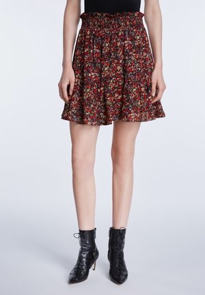 Jupe florale noire avec une taille smockée, ornée de fleurs rouges, jaunes et vertes sur un fond sombre. Associée à des bottines noires.