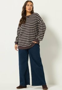 Sweat-shirt à manches longues rayé de couleur marron foncé avec des rayures crème, associé à un jean bleu à jambes larges et des chaussures marron à enfiler.