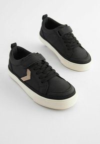 Černé tenisky s textilním koženým svrškem, vybavené suchým zipem, šněrovacím designem a krémovou gumovou podrážkou. Doplňuje je béžové logo.