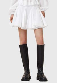 Witte geplooide rok met een aansluitende tailleband, gecombineerd met elegante zwarte kniehoge laarzen met een gladde afwerking en een gestructureerde zool.