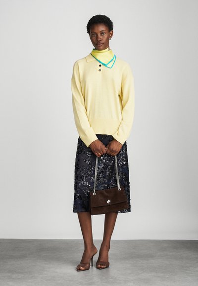 Jersey amarillo de punto con dos botones, superpuesto a un cuello de tortuga verde brillante. Falda de lentejuelas azul marino, bolso de ante marrón y tacones marrones.