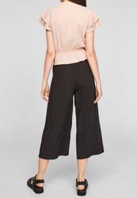 Top texturizado rosa claro con mangas de volantes, combinado con pantalones de pierna ancha negros. Sandalias negras con detalles en las correas completan el look.