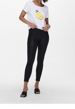 T-shirt blanche avec un graphique de citron jaune, associé à des leggings noirs à motif et des sandales à glissière noires. Les leggings présentent un imprimé animal discret.