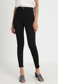 Jean skinny noir taille haute en denim avec fermeture éclair et bouton, doté de quatre poches et d'une texture lisse.