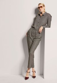 Schwarz-weiße gemusterte Bluse und passende pants mit lockerer Passform, ergänzt durch dunkelrote spitze Absätze und große goldene Ohrringe.