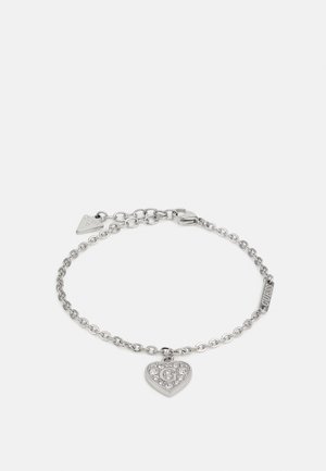 Srebrna bransoletka z łańcuszkiem z zawieszką w kształcie serca wysadzaną kryształkami i inicjałem „G”, z małą metką „Guess” przy zapięciu.