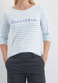 Vaaleansiniset ja valkoiset raidalliset pitkähihaiset paidat, joissa on pyöreä kaula-aukko ja "Marc O'Polo" -teksti tummansinisellä brodeerauksella. Kangas näyttää pehmeältä.