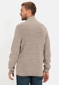 Hellbraunes, strukturiertes Sweatshirt mit hohem Kragen, gerippten Bündchen und lockerer Passform. Trägt es mit dunkelblauen Jeans, von hinten gesehen.