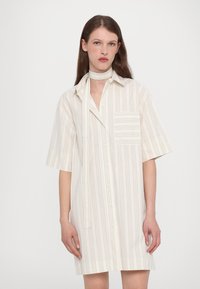 Abito camicia a maniche corte a righe in crema chiaro e beige. Presenta un colletto, chiusura frontale con bottoni e una tasca sul petto. Include una sciarpa coordinata.