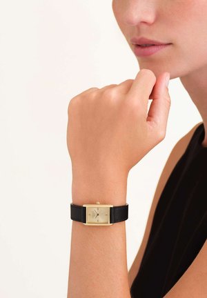Orologio rettangolare dorato con quadrante minimalista, cinturino in pelle nera e finitura testurizzata. Il display mostra gli indicatori delle ore e dei minuti.