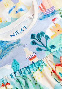 Dětské šaty s potiskem na téma moře, který zahrnuje maják, stromy, pískový hrad, lodě a racky, s bílým kulatým výstřihem.