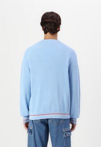 Felpa azzurro chiaro con texture a costine, colletto a girocollo e accenti a strisce rosse e bianche in contrasto sui polsini e sull'orlo.