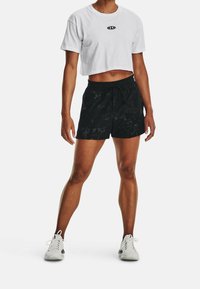 Klippt vit t-shirt med en liten svart logotyp; parat med svarta shorts med en texturerad mönster och dragsko i midjan. Vita träningsskor.