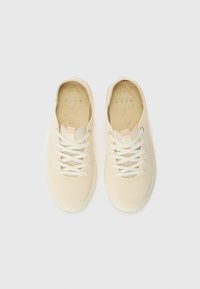 Baskets en maille beige avec une tige texturée, un laçage et une semelle en caoutchouc de couleur claire. Présente un logo minimaliste sur la languette.