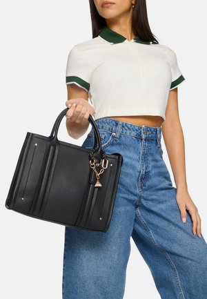 Borsa a tracolla nera testurizzata con doppio manico, decorata con accessori in oro e un ciondolo. La parte anteriore presenta tre cuciture verticali per una maggiore struttura.