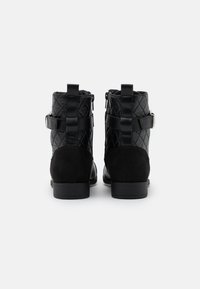 Bottines noires avec un dessus synthétique matelassé et un talon en daim, dotées de zips latéraux et d'une sangle décorative avec une boucle.