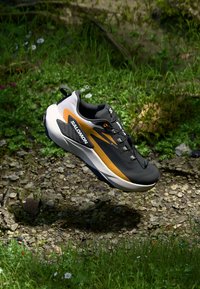 Chaussure de course Salomon en gris, noir et orange. Design léger avec une tige texturée, une semelle rembourrée et un logo bien visible.