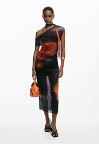 Robe dégradé noire et orange avec une épaule, texture transparente et fente haute sur la cuisse. Assortie à un sac à main orange et des sandales noires.