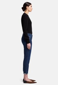 Zwarte lange mouwen top, slim-fit blauwe jeans en puntige flats met luipaardprint. Casual outfit met een getailleerd silhouet en opgerolde mouwen.