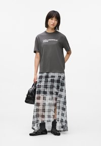 Camiseta gris con la impresión "KARL LAGERFELD JEANS", superpuesta sobre una falda maxi de cuadros transparente en blanco y negro, combinada con zapatos negros y un bolso.