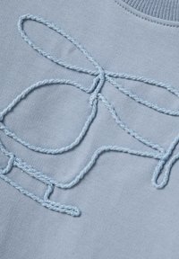 Maglione azzurro chiaro con un design ricamato di anelli intrecciati e fiocchi in un filo di azzurro più chiaro, creando un motivo testurizzato.
