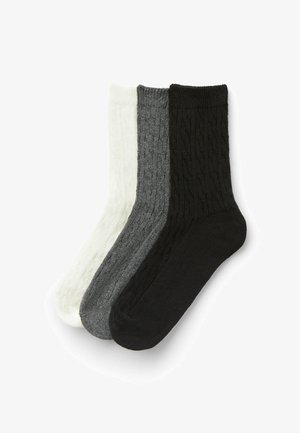 Trois paires de chaussettes en tricot de couleur blanche, grise et noire. Le design présente un motif côtelé texturé, avec une finition douce.