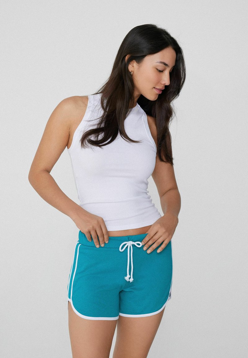 Top senza maniche bianco a costine e pantaloni corti teal con bordi bianchi e coulisse. I pantaloni corti presentano strisce laterali e una vestibilità rilassata.