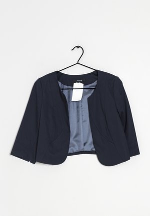 Marineblå cropped blazer med trekvartærmer på en sort bøjle, mod en ensfarvet hvid baggrund.