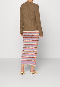 Ruskea neulottu pusero pyöreällä pääntiellä, yhdistetty moniväriseen raidalliseen hameeseen, jossa on vaaleanpunaisia, sinisiä ja keltaisia yksityiskohtia.