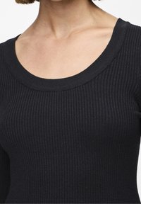 Black ribbed long-sleeve top featuring a wide, rounded neckline and a fitted silhouette, showcasing a smooth texture and subtle stretch.