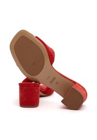 Sandali con tacco alto in suede rosso, con tacco a blocco e retro aperto. La suola è beige con dettagli del marchio in rilievo. Texture liscia in tutto il prodotto.