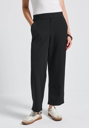 Black wide-leg trousers made of soft fabric, featuring side pockets and a smooth waistband. Paired with casual sneakers.