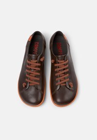 Zapatos de cuero marrón con un acabado suave, que presentan cordones naranjas y suelas de goma en contraste. Inscripción "CAMPE" visible en rojo en el interior.