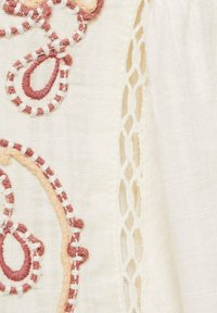 Biely textil s výšivkami kvetinových motívov v ružovej a broskyňovej farbe, doplnený čipkovým lemom s otvoreným tkaním.