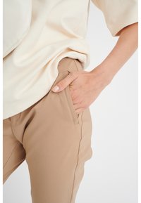 Beige skräddarsydda byxor med sidofickor, tillsammans med en lös passform i off-white topp. Tyget verkar slätt och något texturerat.