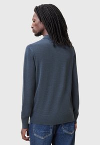 Mørkeblå langærmet sweater i blødt strikmateriale med ribkant ved krave og manchetter, parret med denim jeans med baglommer.