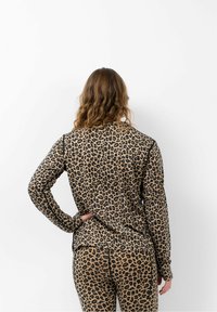 Langärmliges Oberteil mit Leopardenmuster und passenden Leggings, hergestellt aus einem weichen Material und in figurnaher Passform, mit schwarzen Akzenten entlang der Nähte.