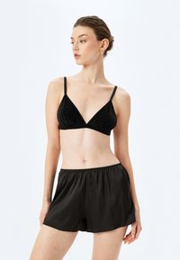 Bralette negro con tejido texturizado y escote en V, combinado con pantalones cortos de satén negros con cintura elástica y corte holgado.