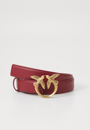 Burgundy leather belt featuring a round gold buckle with two intricately designed birds. Smooth texture, minimalist design, and adjustable length.