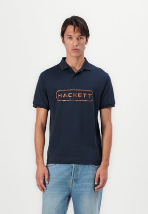 Polo shirt bleu marine en coton, avec un logo "HACKETT" orange contrastant sur le devant et un col classique. Coupe décontractée avec des manches courtes.