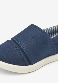 Navyfarbene Canvas-Slipper verfügen über ein gepolstertes Obermaterial, eine weiße Gummisohle und ein gestreiftes Stofffutter. Das Design beinhaltet subtile Steppdetails.