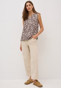 Haut beige sans manches avec un imprimé léopard brun foncé, associé à un pantalon beige clair ample et des chaussures brunes à enfiler.